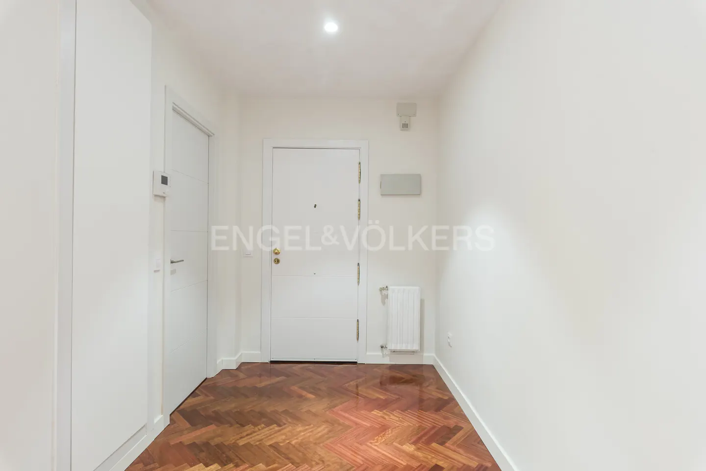 A bright, white entryway with a wood parquet floor, a white front door, and a white storage closet.