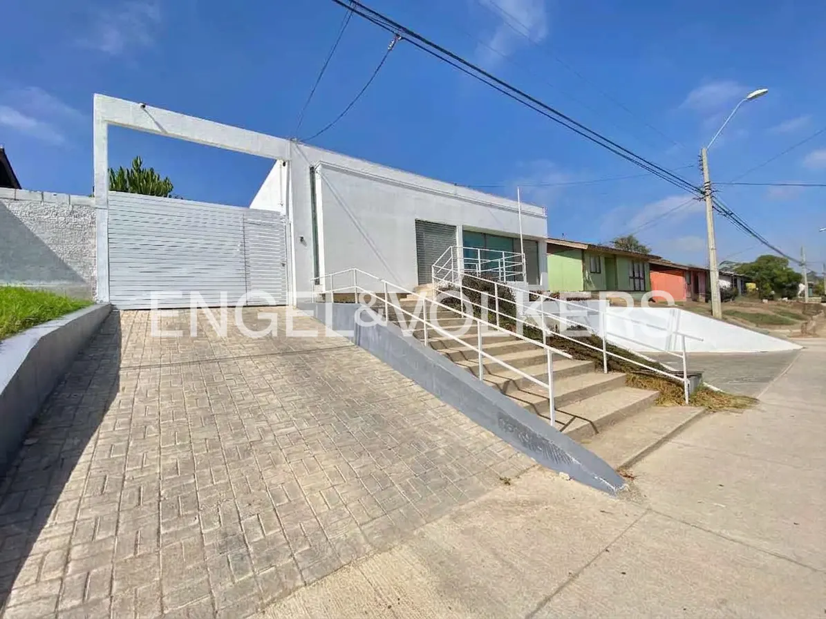 Exterior view of a modern, white, one-story house with a gated driveway and stairs leading to the entrance.