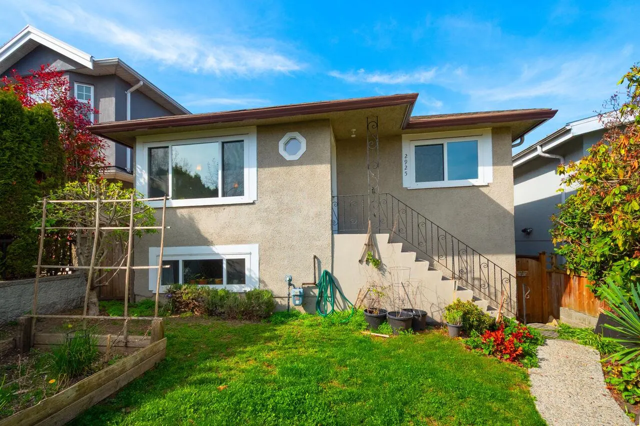 Beige two-story house with white-framed windows, a small round window, and a staircase leading to the front door. Green lawn and blue sky.