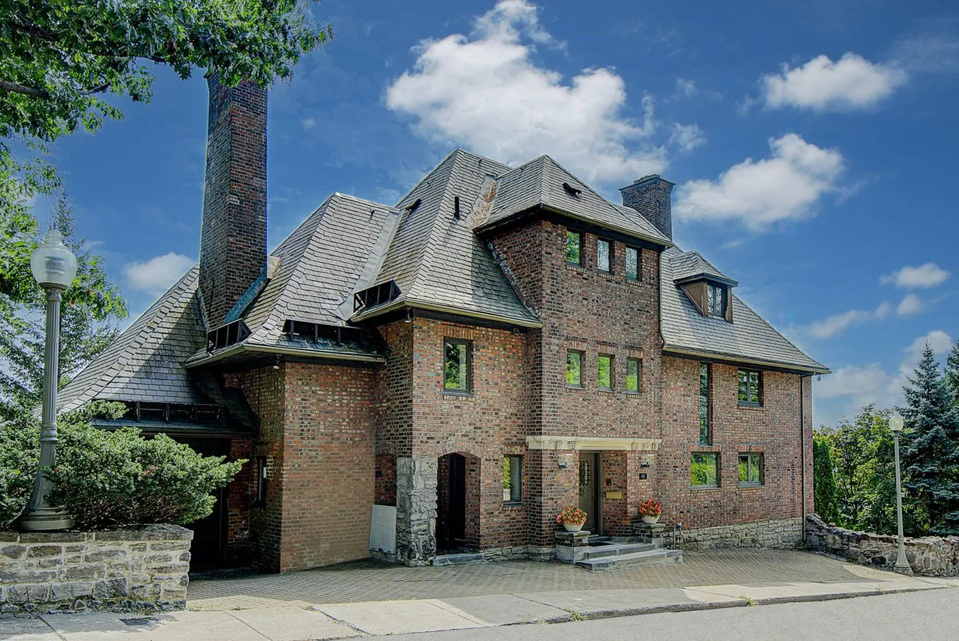 Exterior view of a large, two-story brick house with a complex roofline and tall chimney under a blue sky with scattered clouds.