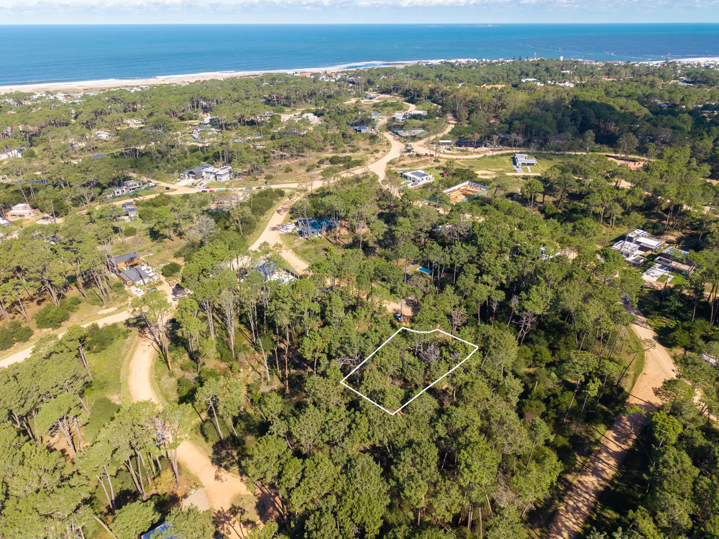 Aerial view of a wooded lot outlined in white, near a beach and ocean under a blue sky.