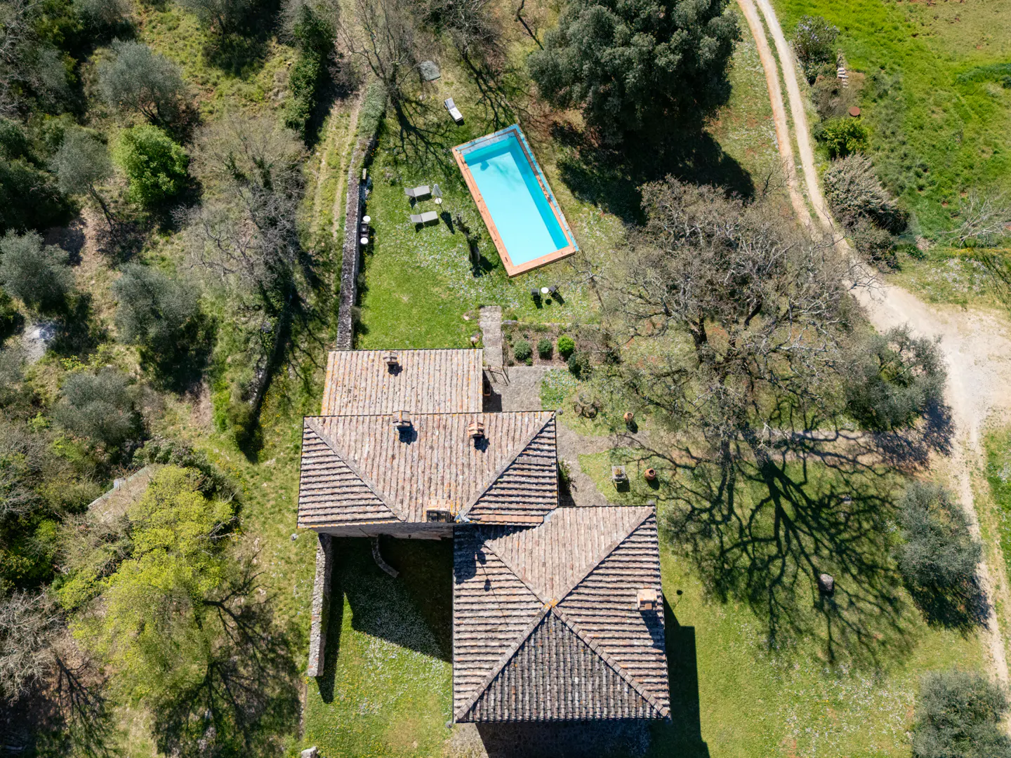 Aerial view of a terracotta-roofed house with a blue rectangular pool, green lawn, and trees.