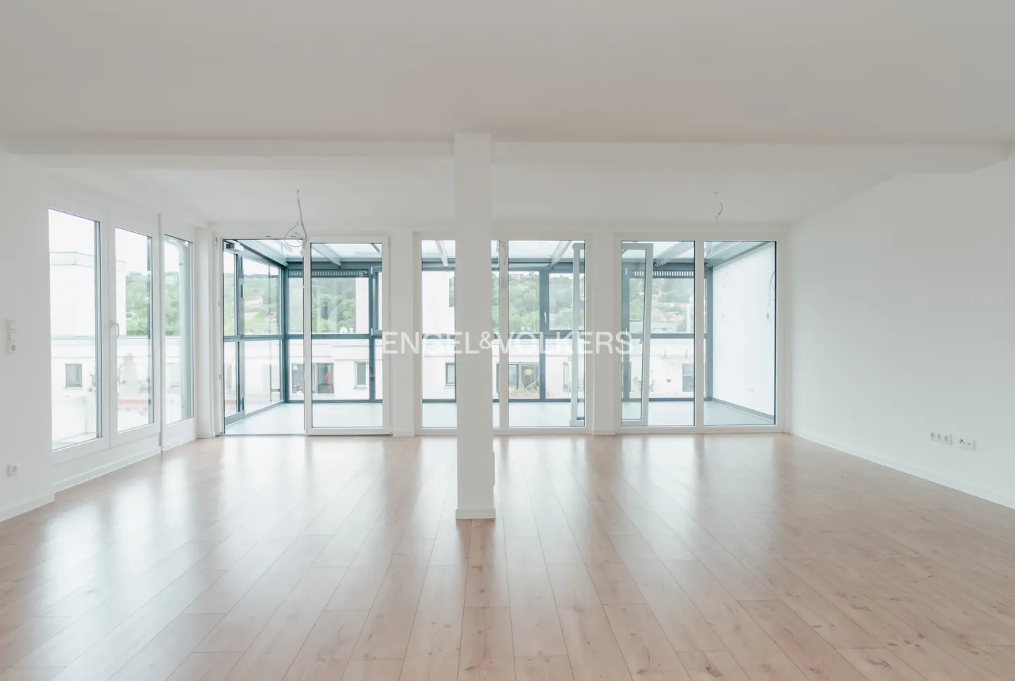 Bright, empty room with light wood floors, white walls, and large floor-to-ceiling windows leading to a balcony.