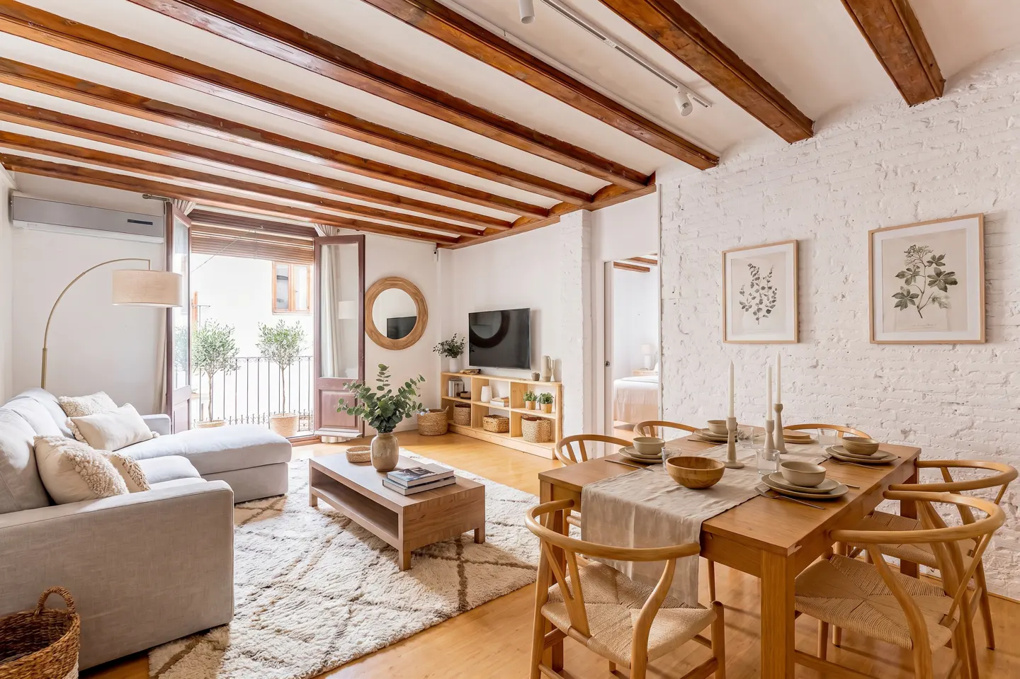 Bright living room with exposed wood beams, white brick walls, and a balcony. A dining table is set for a meal.