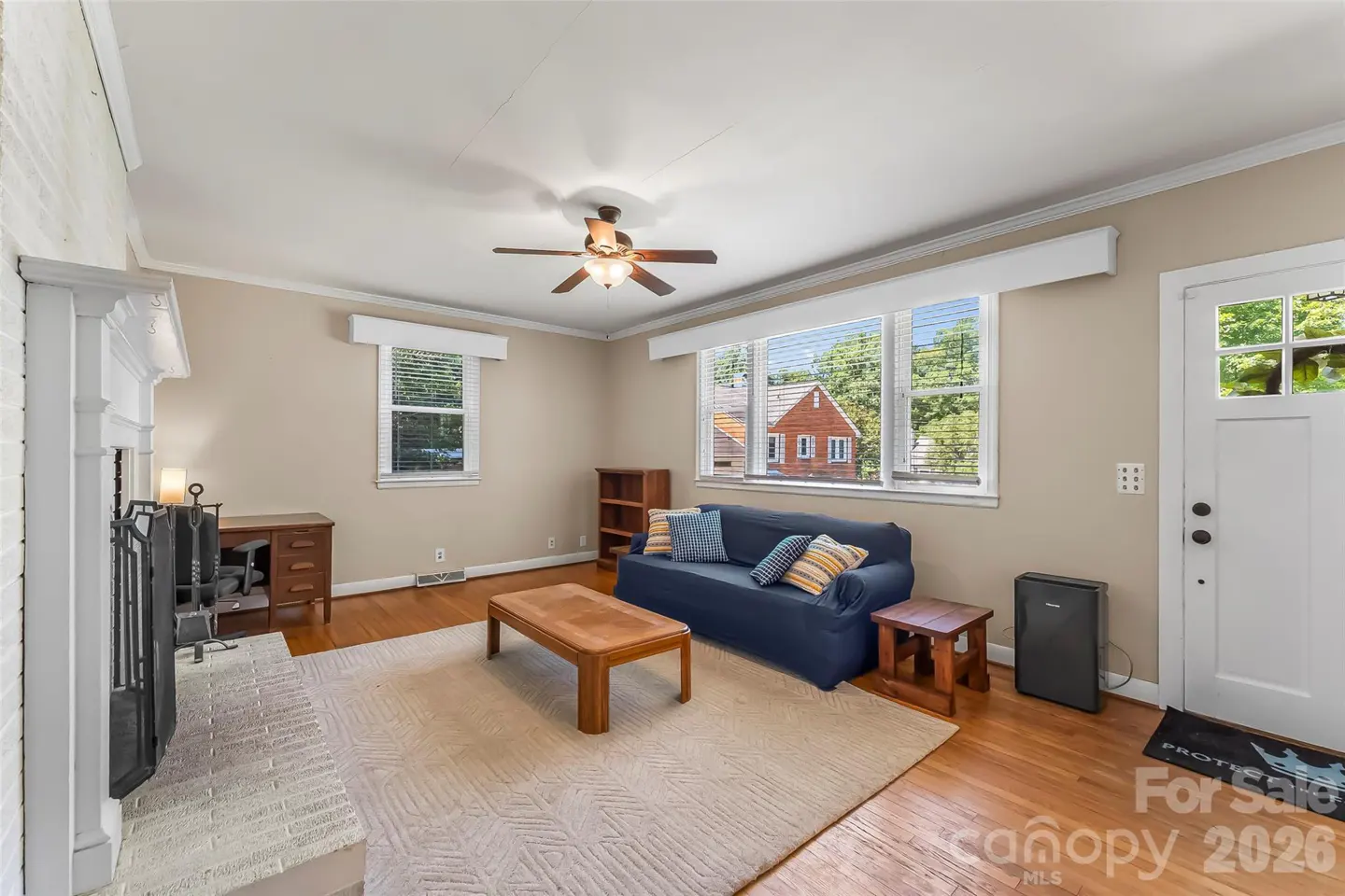 Living room with hardwood floors, a blue sofa, wooden coffee table, white fireplace, and a white door leading outside.