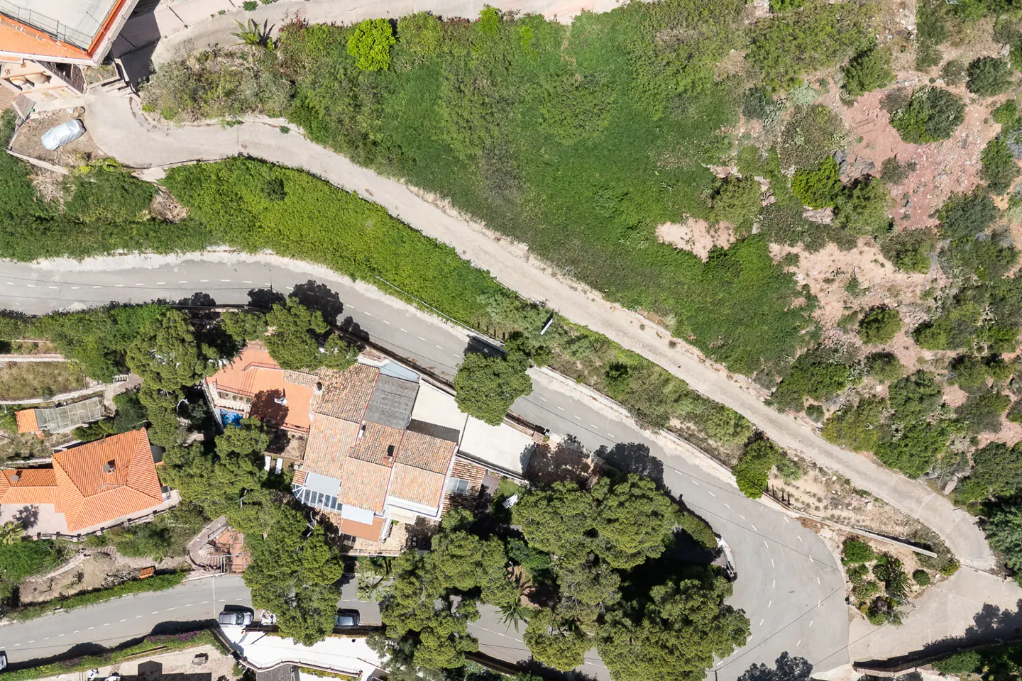 Aerial view of houses with orange tile roofs, green trees, and winding roads on a sunny day.