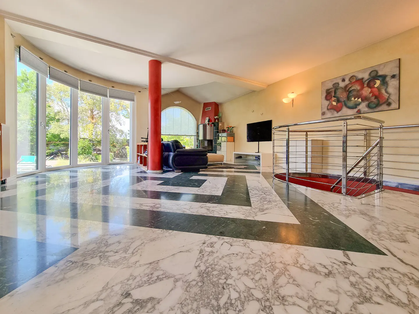 A spacious living room with marble floors, large windows, and a red support column.