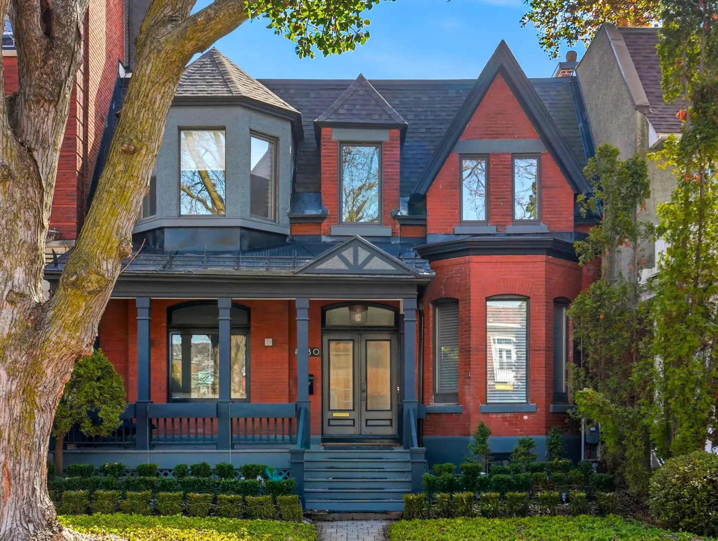 Exterior of a red brick house with a gray porch, black roof, and green lawn.