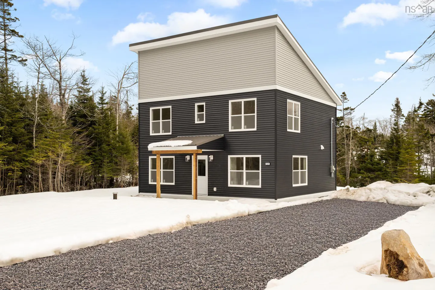 Two-story house with gray siding on top and dark siding on the bottom, surrounded by trees and snow.