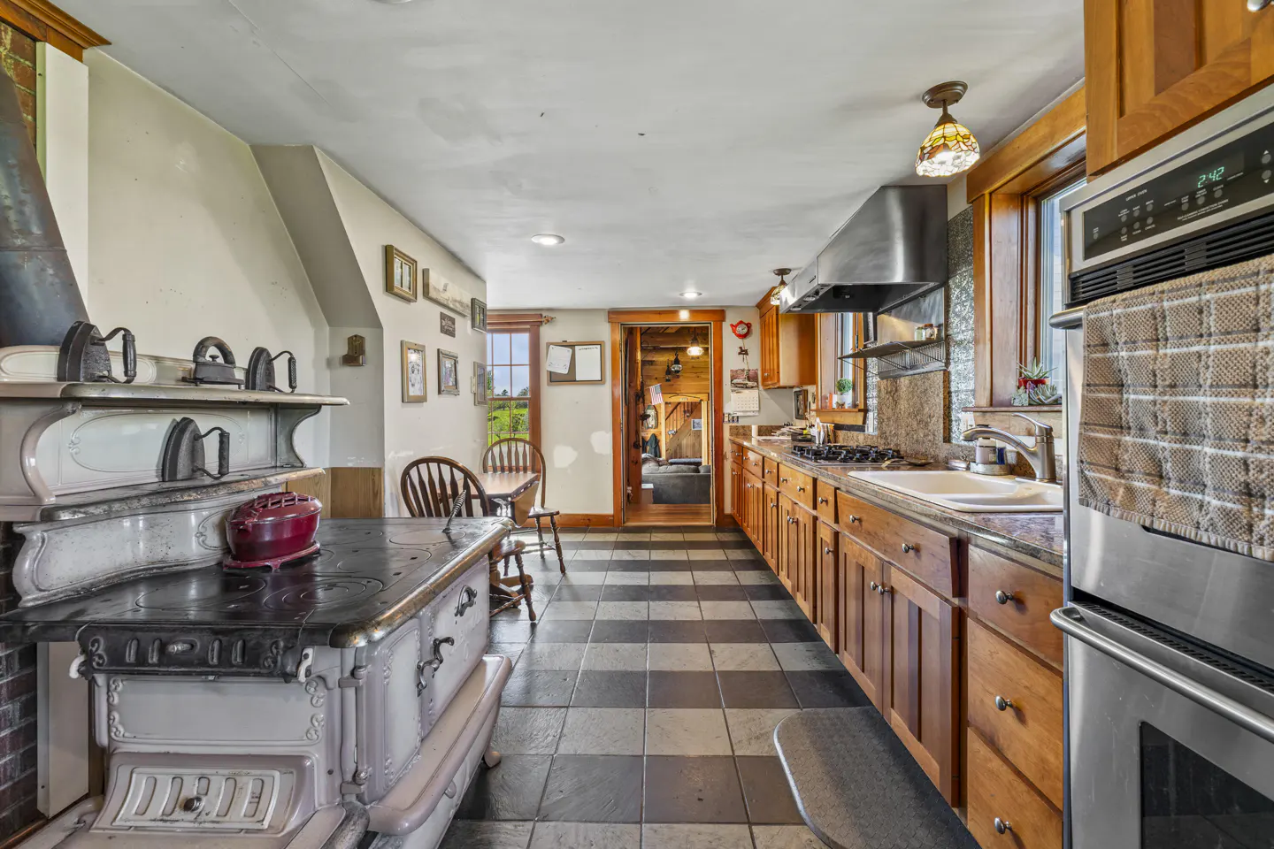 A farmhouse kitchen with black and white tile floors, wood cabinets, and an antique stove.