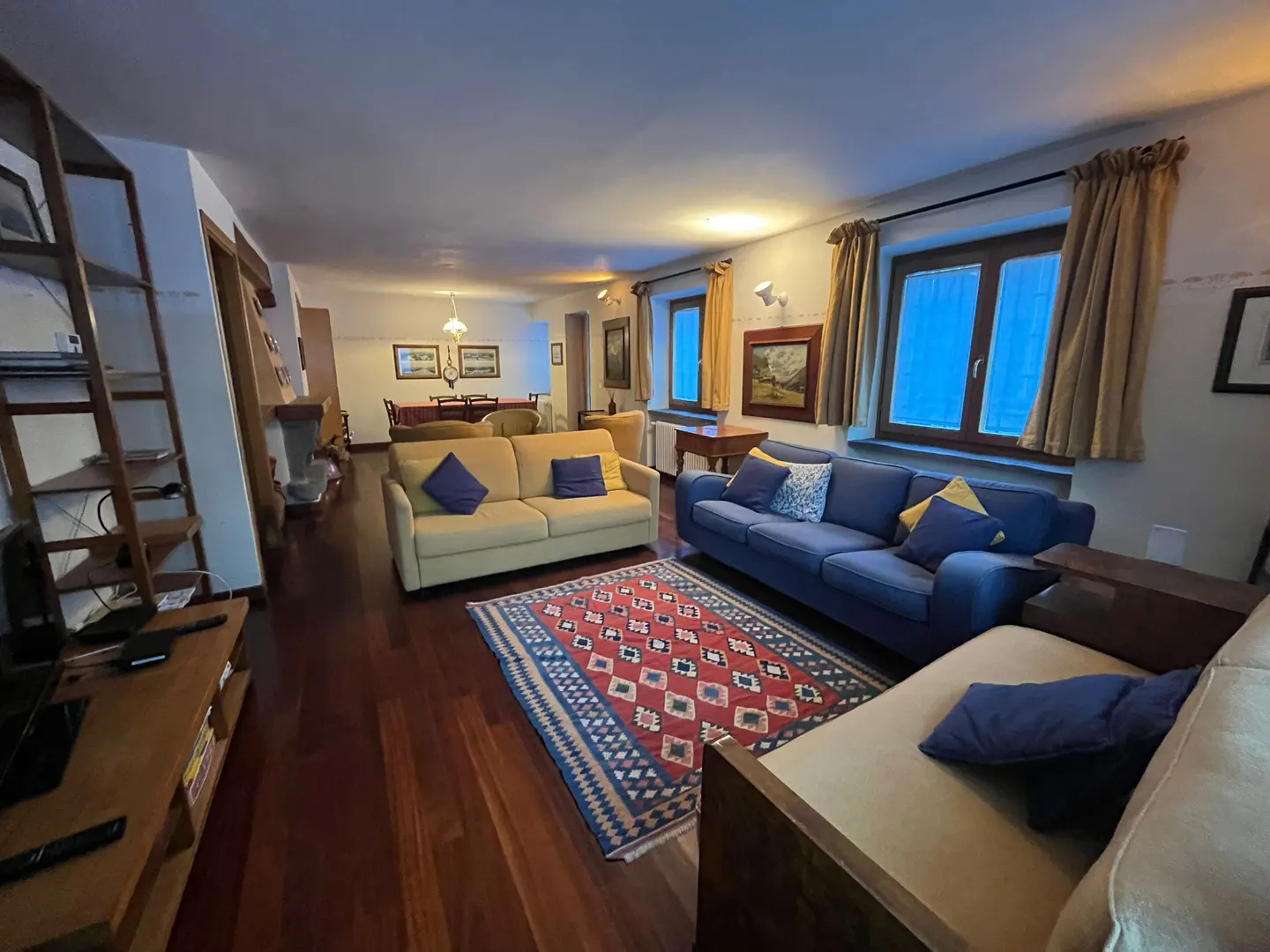 Spacious living room with hardwood floors, a blue sofa, a yellow sofa, and a colorful patterned rug in the center.