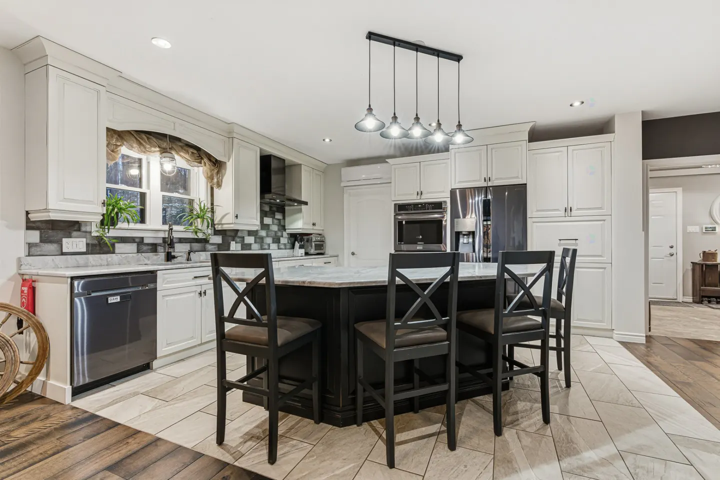 A modern kitchen with white cabinets, a black island with bar stools, and stainless steel appliances.
