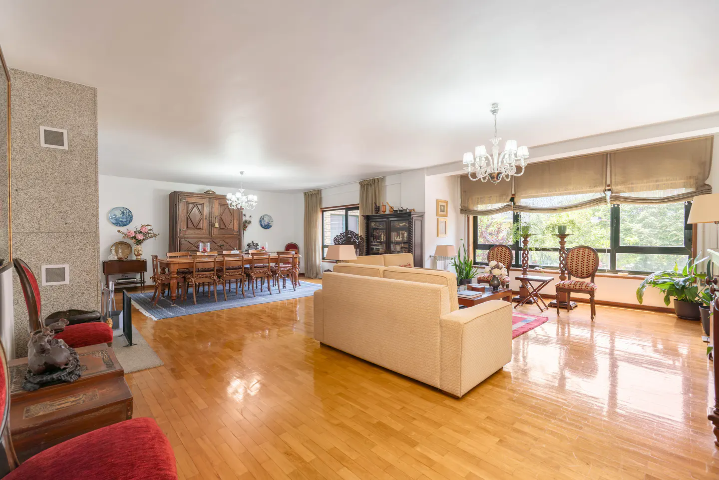 Bright, open-concept living and dining area with hardwood floors. Beige sofa, wood dining table with chairs, and large windows with natural light.