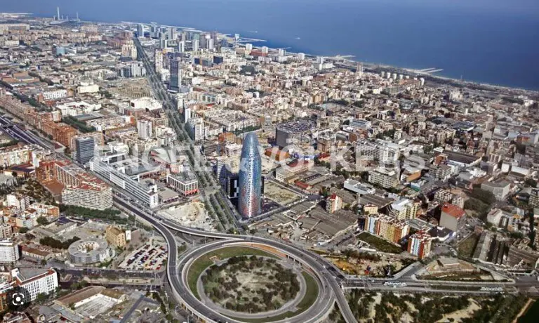 Aerial view of Barcelona, Spain, featuring the Agbar Tower, city buildings, and the Mediterranean Sea in the background.