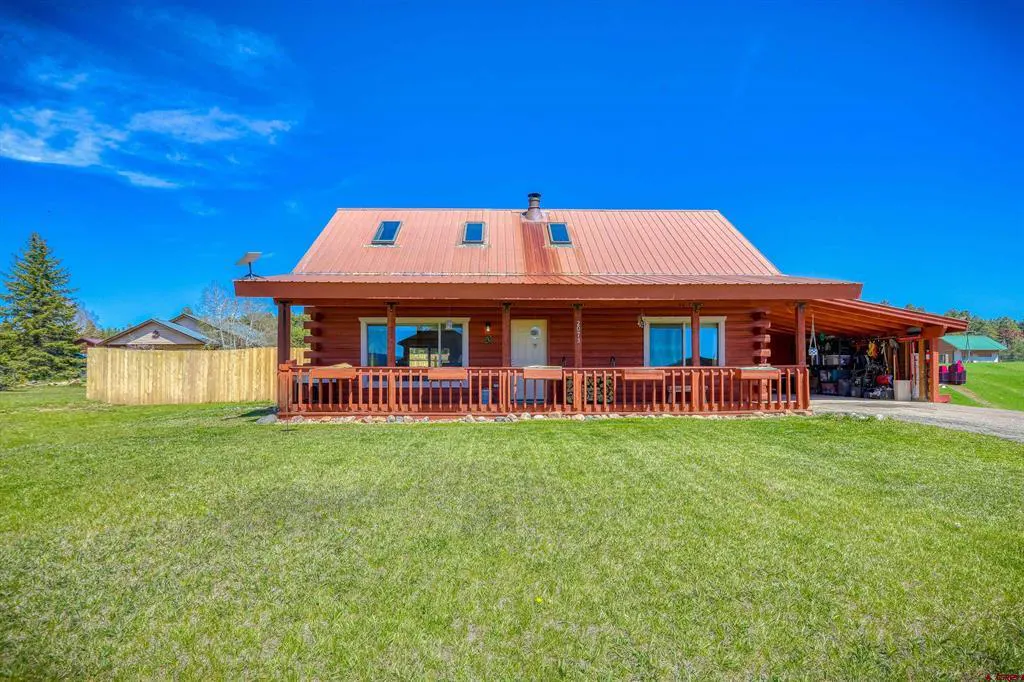 A log cabin-style house with a red metal roof and a covered porch, set against a bright blue sky.