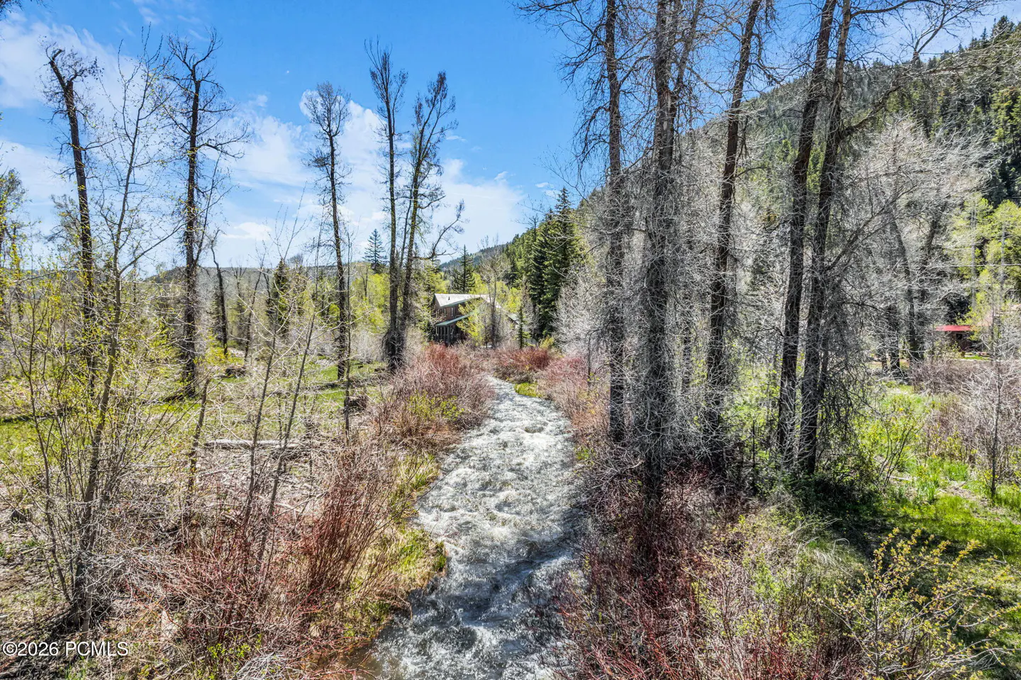 Scenic view of a stream flowing through a wooded area with bare trees and a blue sky.