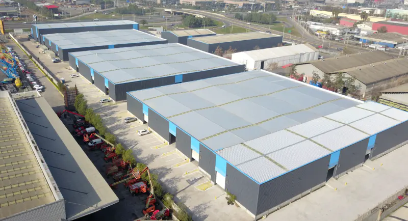 Aerial view of gray industrial buildings with blue trim, parking lots, and construction equipment.