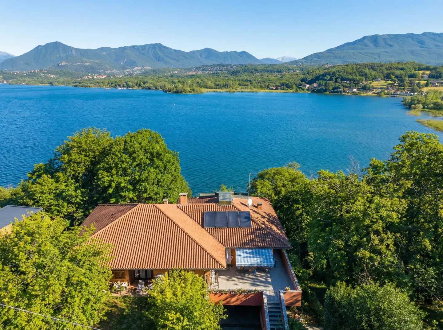 Aerial view of a house with a red tile roof, solar panels, and a patio overlooking a blue lake and mountains.
