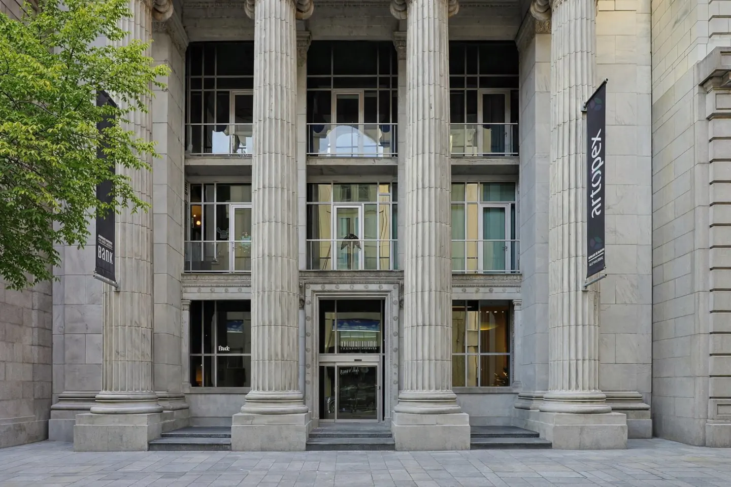 Exterior of a stone building with tall columns and large windows. Banners hang on either side of the entrance.