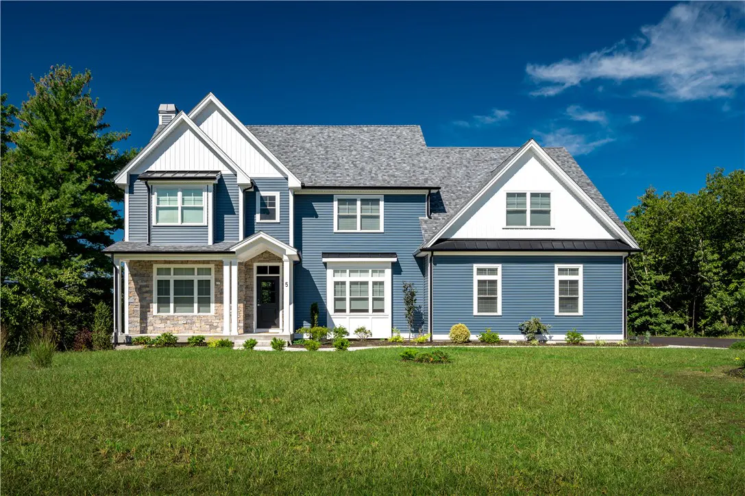 Two-story blue house with white trim and a gray roof on a green lawn under a blue sky.