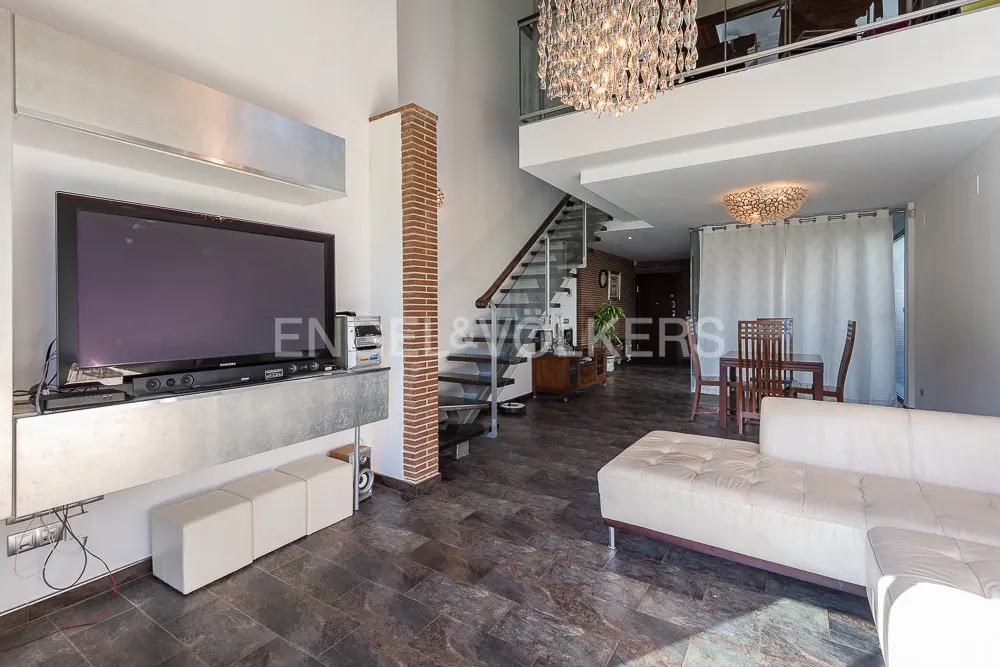 A modern living room with a large TV, white sofa, and a spiral staircase leading to a loft area with a chandelier.
