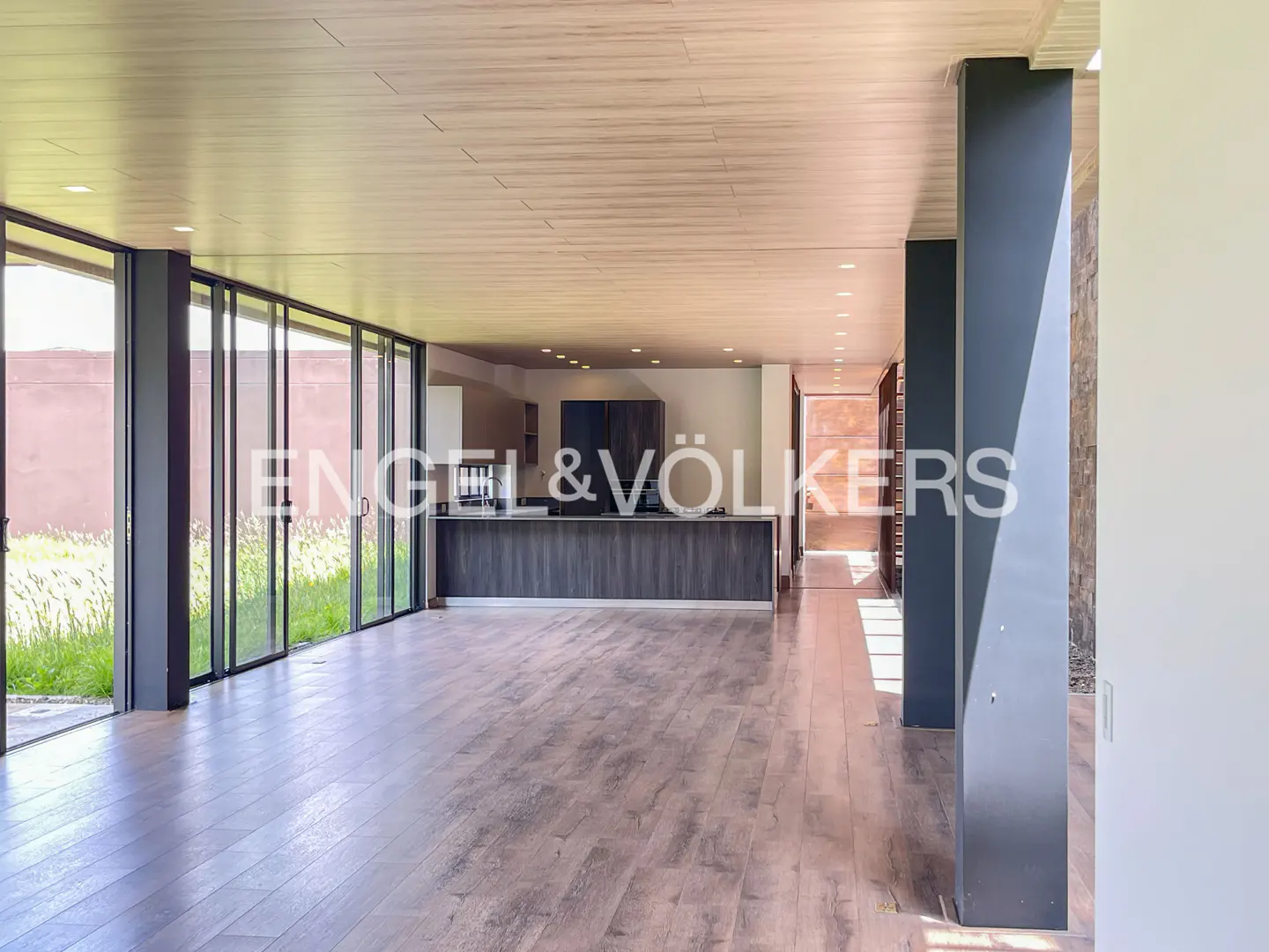 An open-concept home interior with wood floors, a kitchen island, and floor-to-ceiling windows.