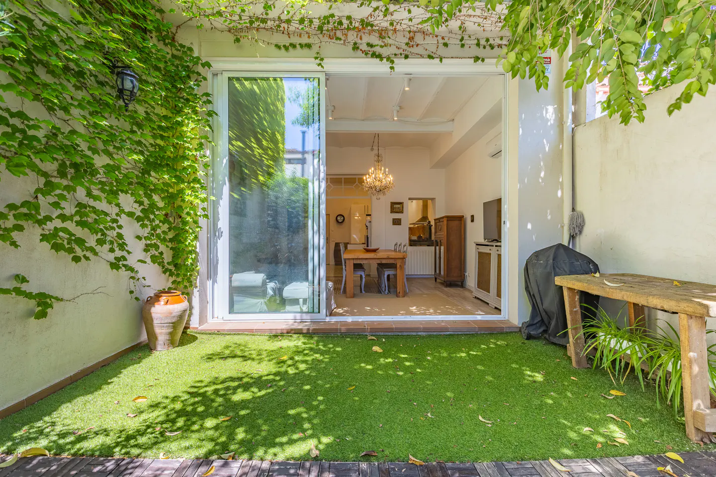 A patio with green grass and a wooden table, leading to an open sliding glass door into a dining room.