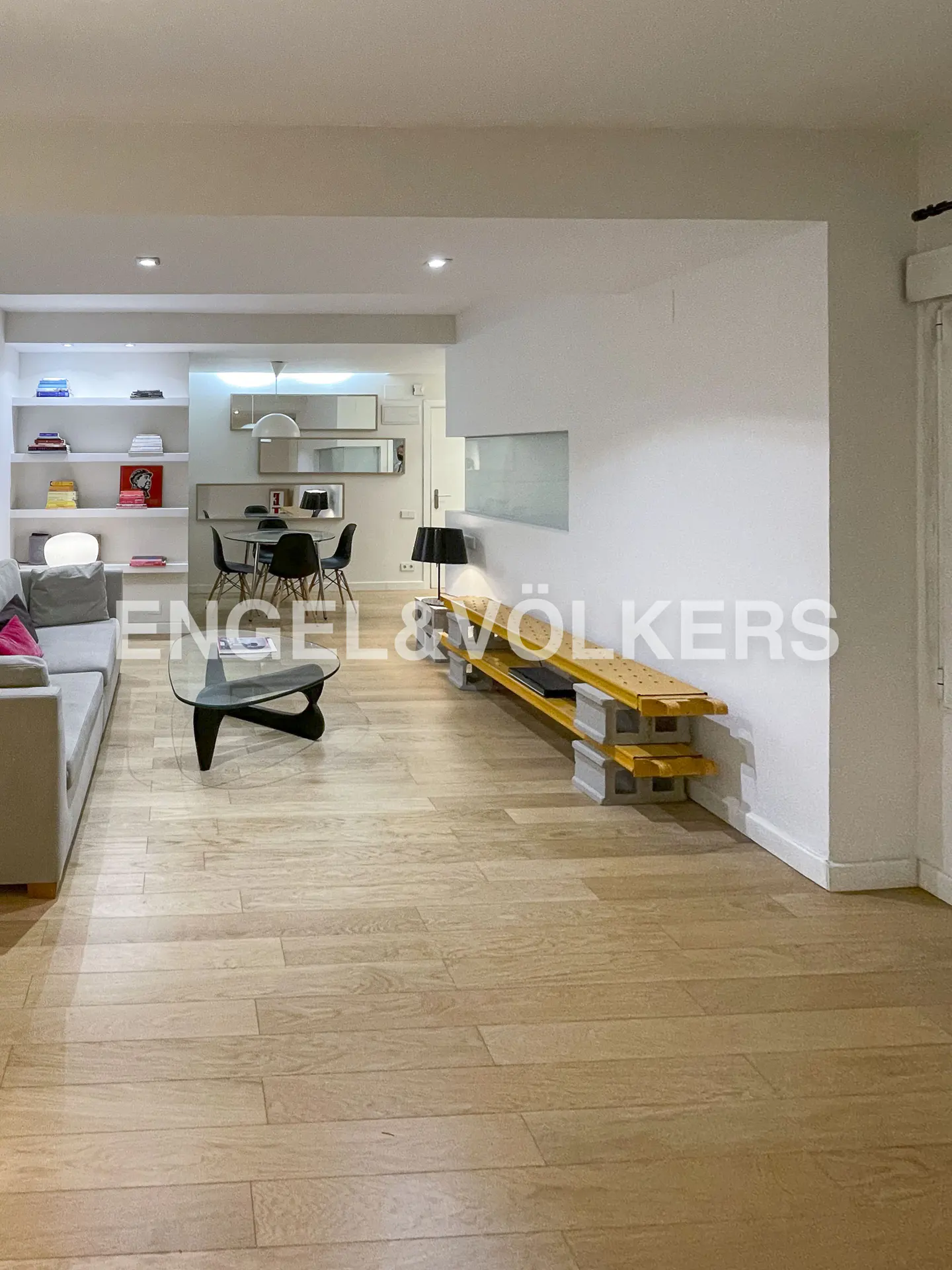 Open-concept living space with light wood floors, gray sofa, glass coffee table, and dining area with black chairs.