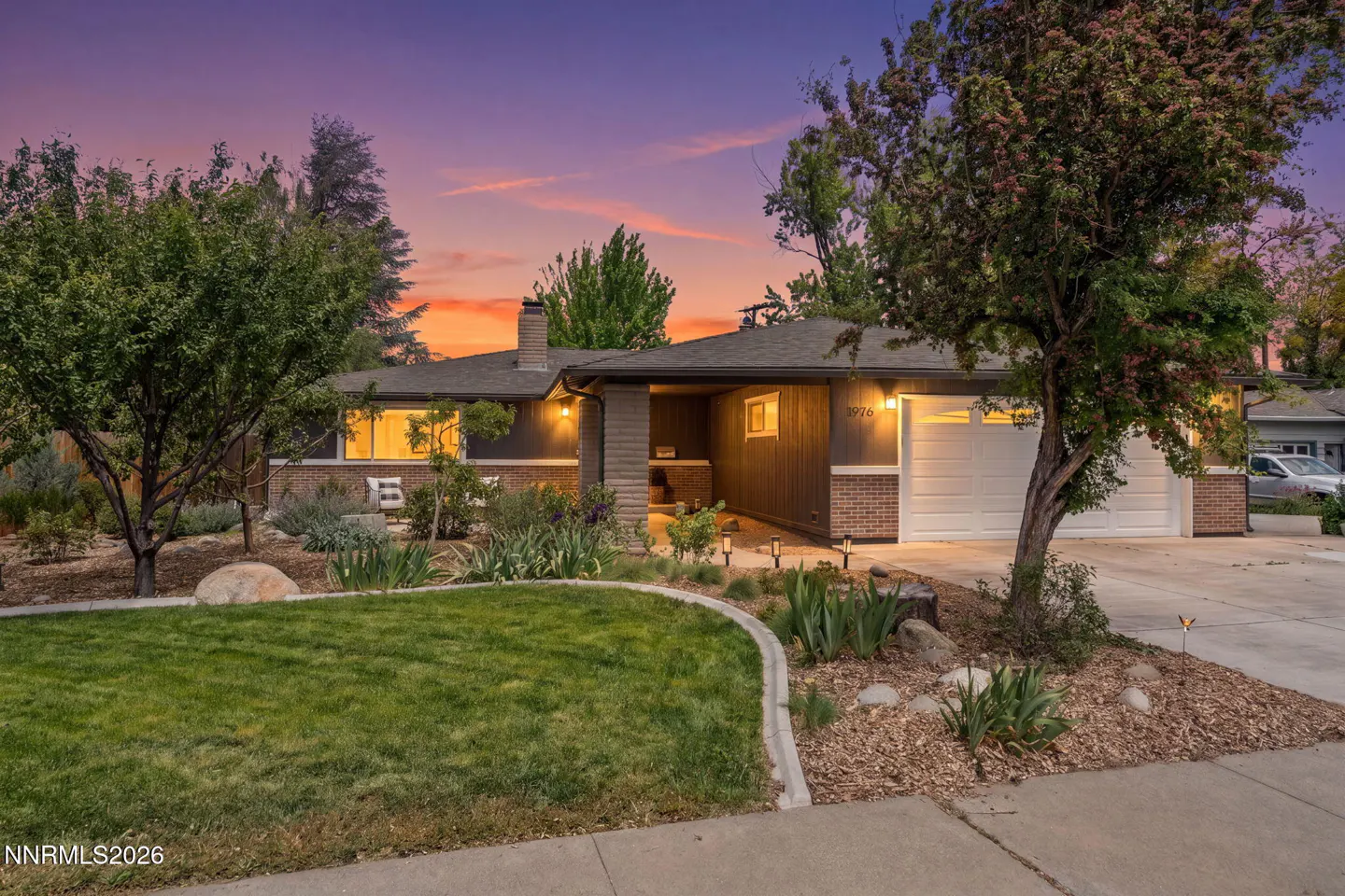 Exterior of a single-story home with a lawn, trees, and a colorful sunset sky.