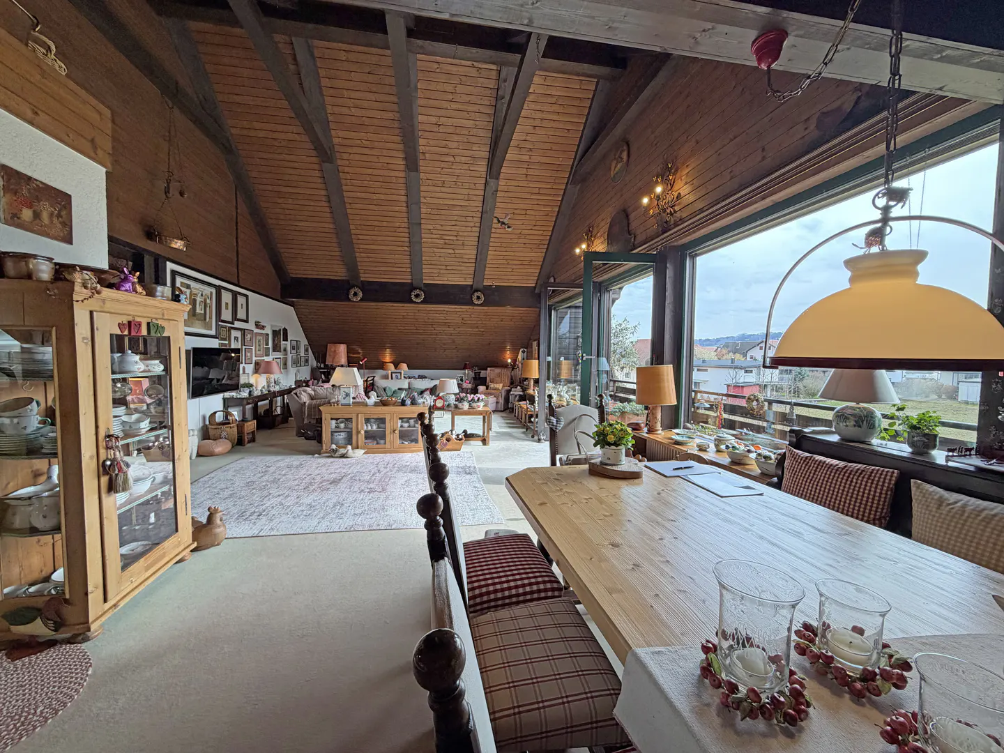 Rustic attic living area with wood-paneled vaulted ceilings, a dining table, and a large window overlooking the outdoors.