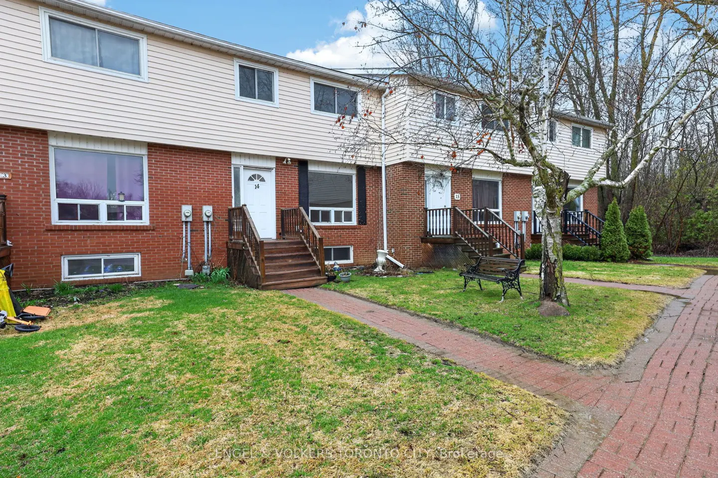 Row of two-story townhouses with brick and beige siding, wooden steps to white doors, and green lawns.