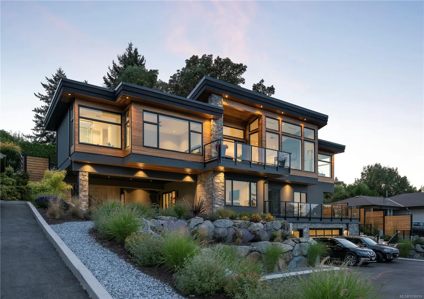 Modern two-story home with wood and gray siding, large windows, and a stone facade. Two black cars are parked in front.