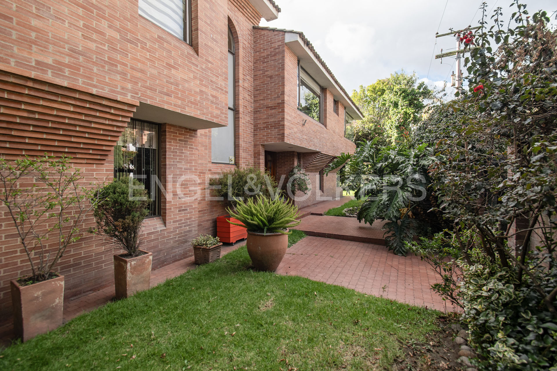 Exterior of a modern red brick house with a green lawn, potted plants, and a paved patio area. [AI-generated text]