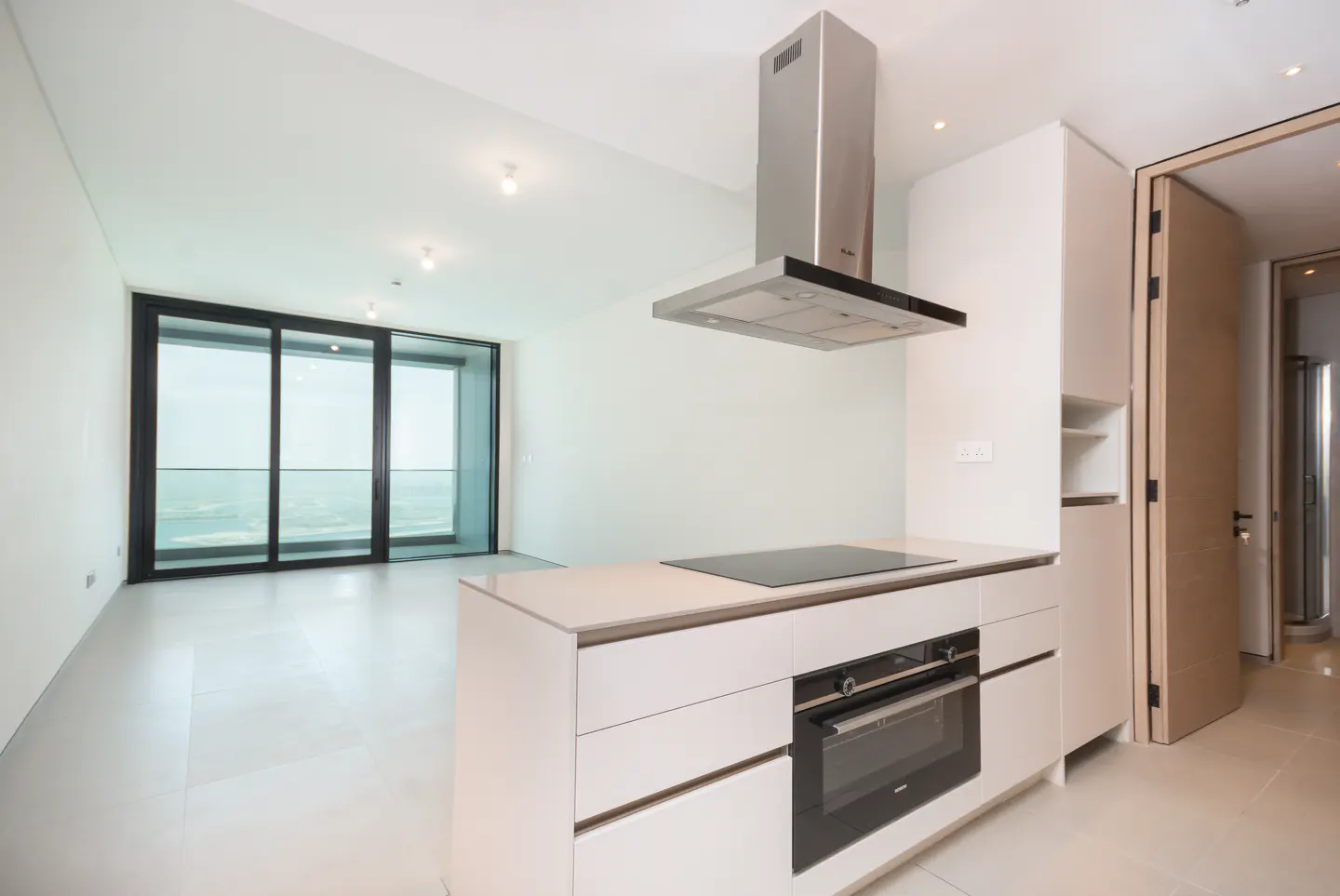 Bright, modern kitchen with white cabinets, stainless steel hood, and black cooktop. Large sliding glass doors offer a view of the ocean.