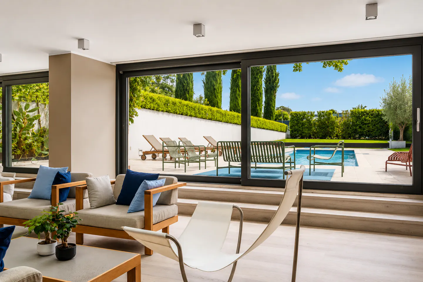 Living room with sofas and a view of a pool and lounge chairs through a large sliding glass door.