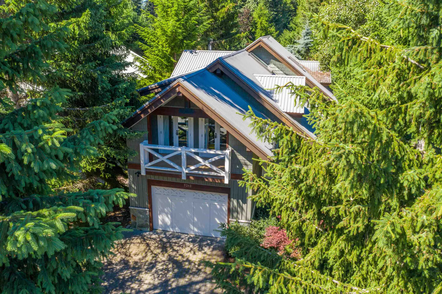 A two-story house with a gray metal roof and white garage door is surrounded by green trees.