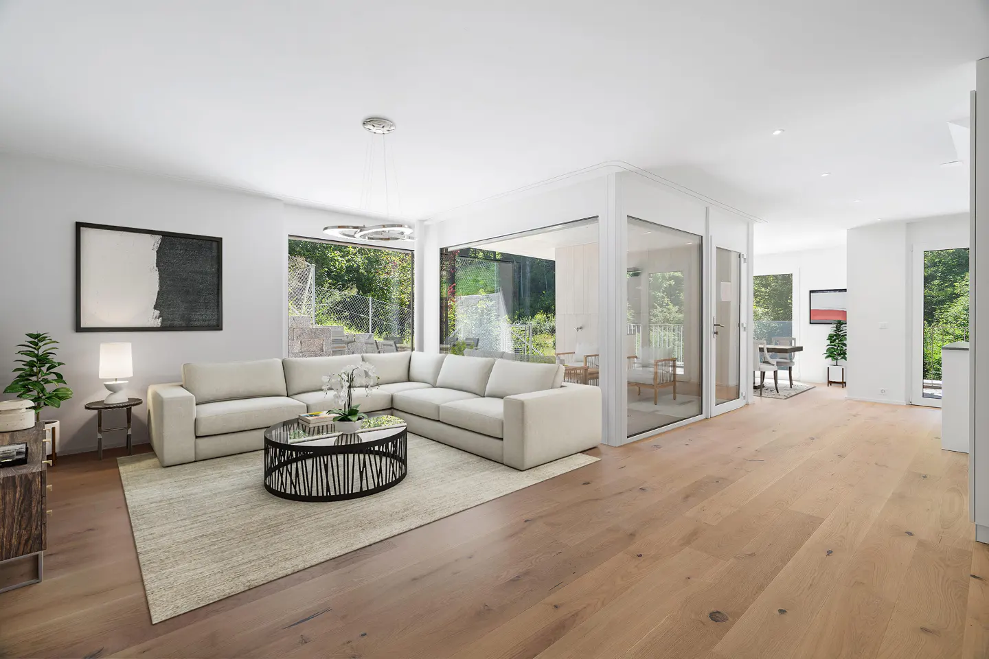 Modern living room with a beige sectional sofa, round coffee table, light wood floors, and a glass-enclosed sunroom.