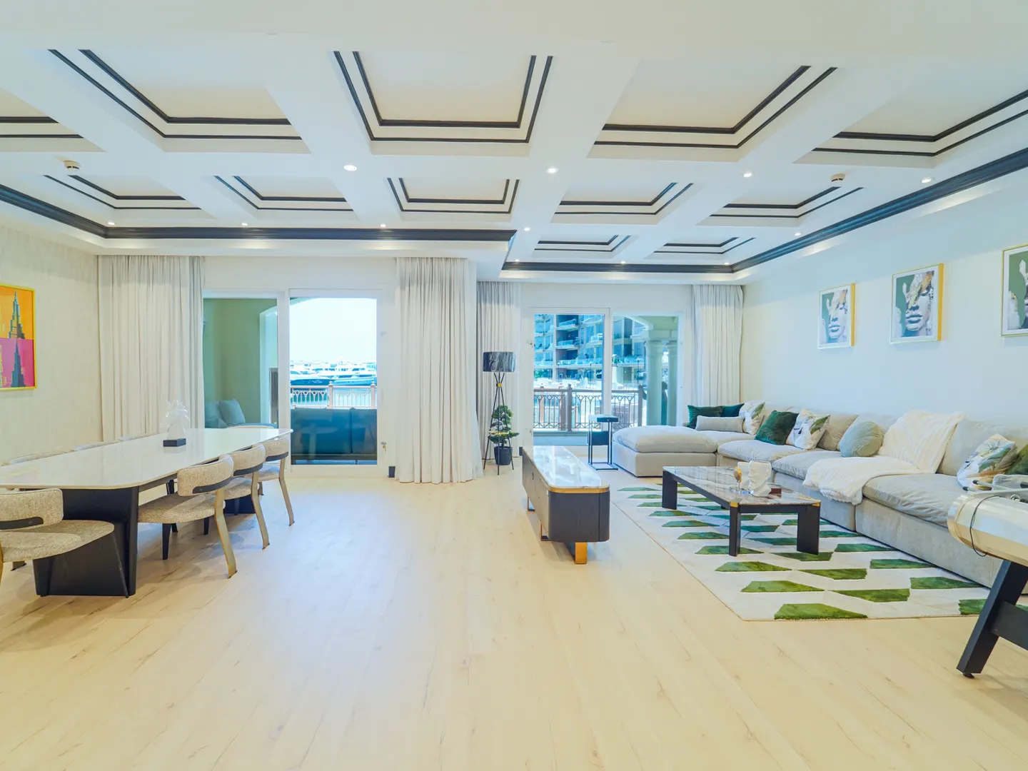 Bright, modern living room with a dining table, large sofa, and balcony views. White walls and light wood floors create an airy feel.