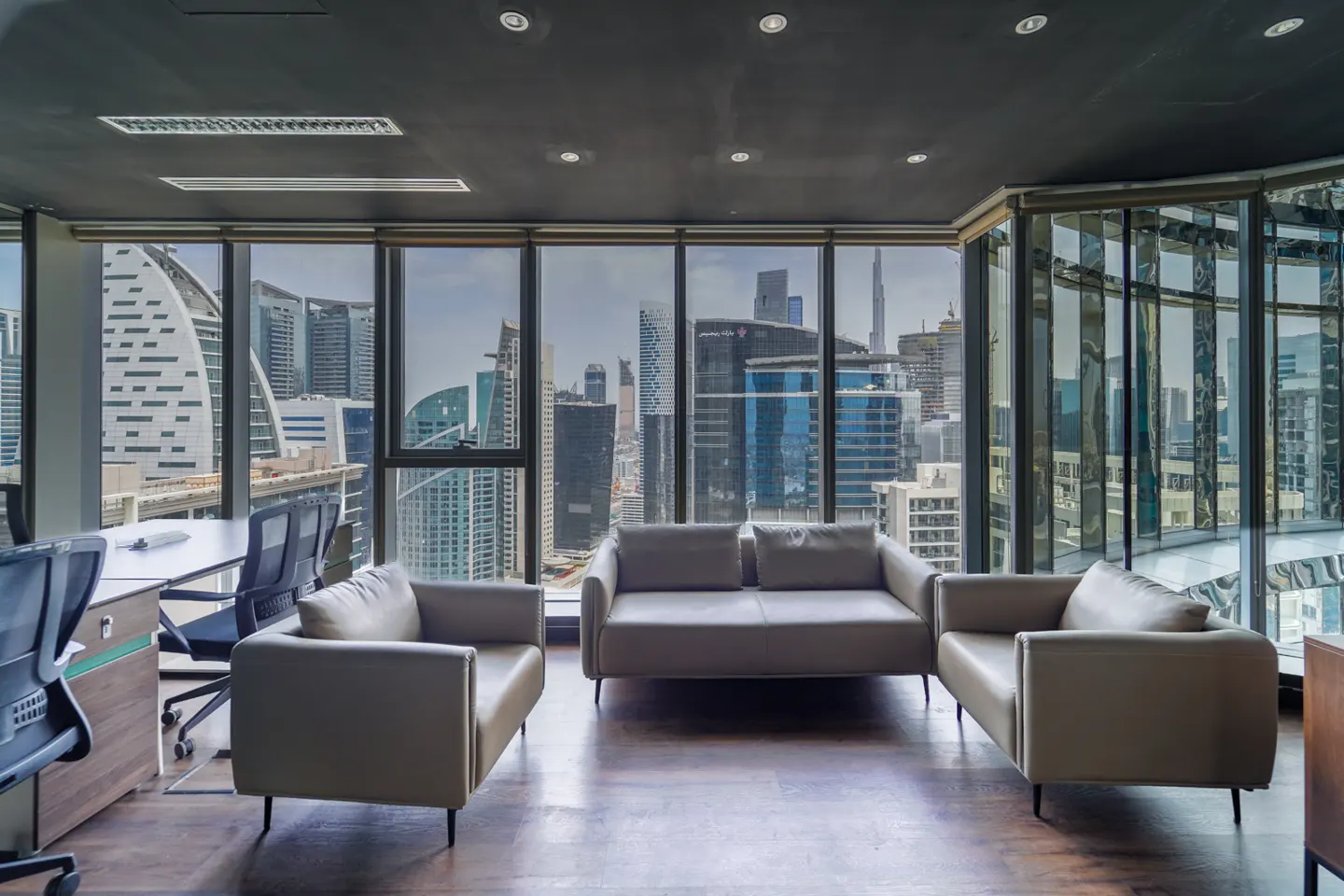 Office lounge area with gray sofas and a city view through large windows. Dark wood floor and ceiling.