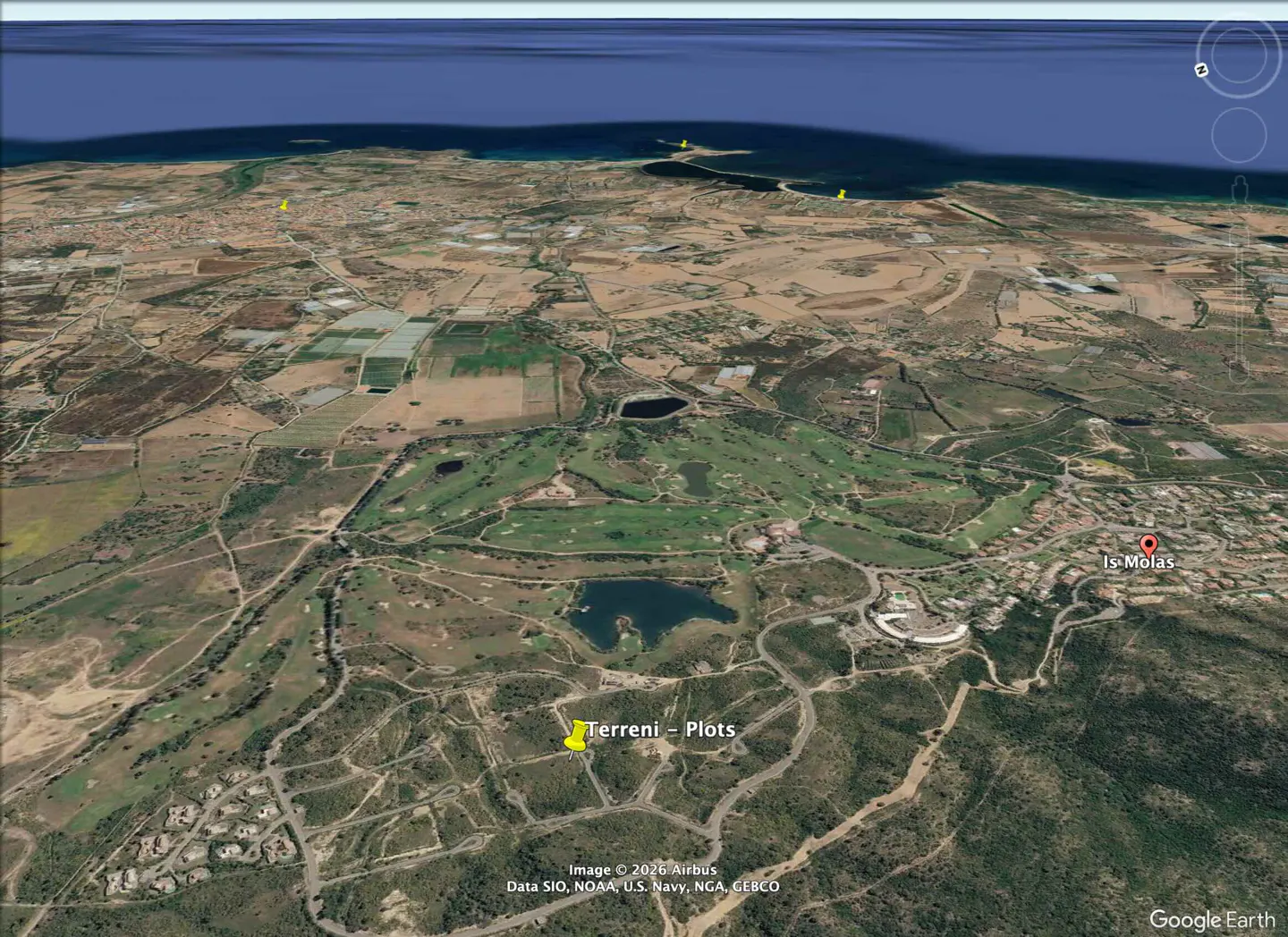 Aerial view of Is Molas, Italy, showing plots of land, a golf course, and the coastline with blue water.
