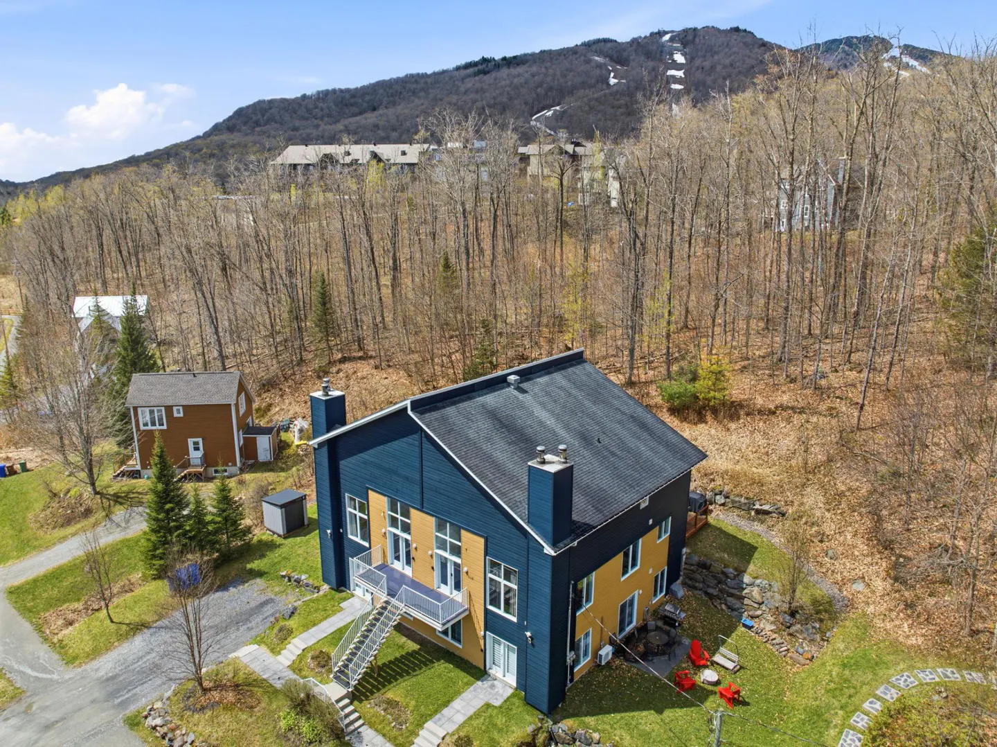 Aerial view of a modern two-story home with blue and yellow siding, a black roof, and a mountain backdrop.