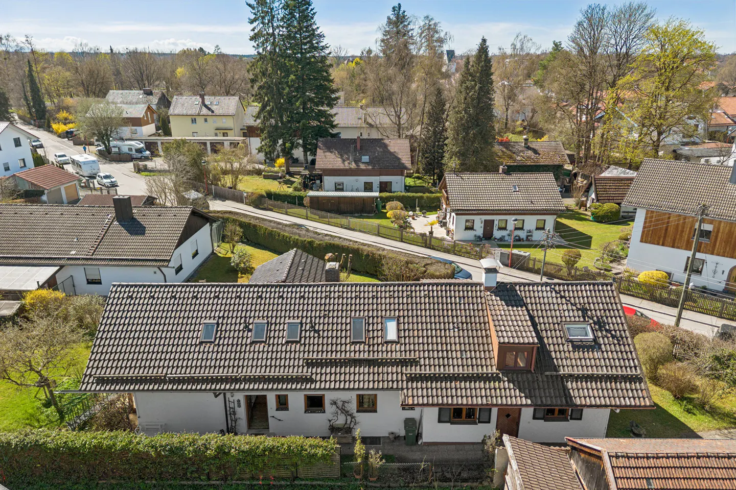 Aerial view of a white house with a brown tiled roof, surrounded by green trees and other houses in a neighborhood.