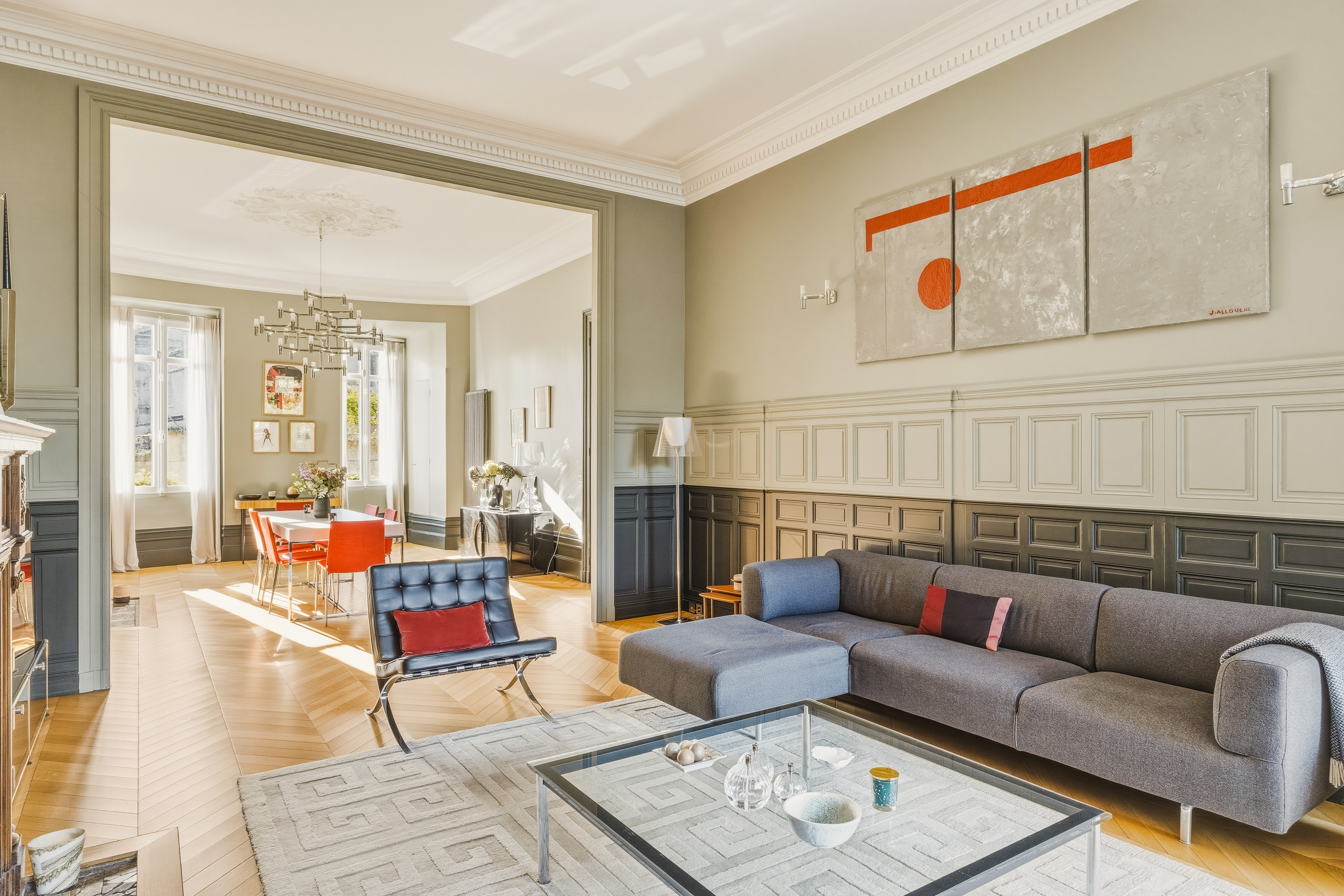 Modern living room with a grey sofa, black leather chair, glass coffee table, and abstract art on a paneled wall. [AI-generated text]