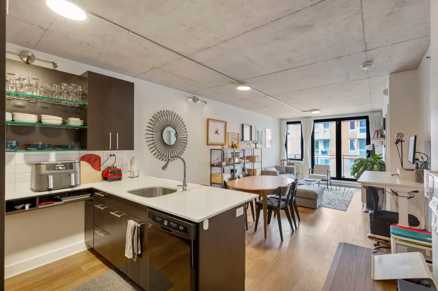 Modern open-concept kitchen and living area with dark cabinets, white countertops, dining table, and concrete ceiling.