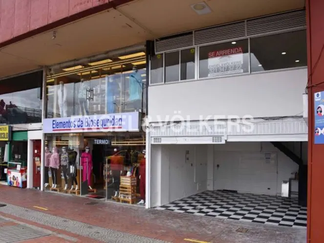 Storefront with "Elementos de Bioseguridad" sign, mannequins in window, and "Se Arrienda" sign above a garage with black and white checkered floor.