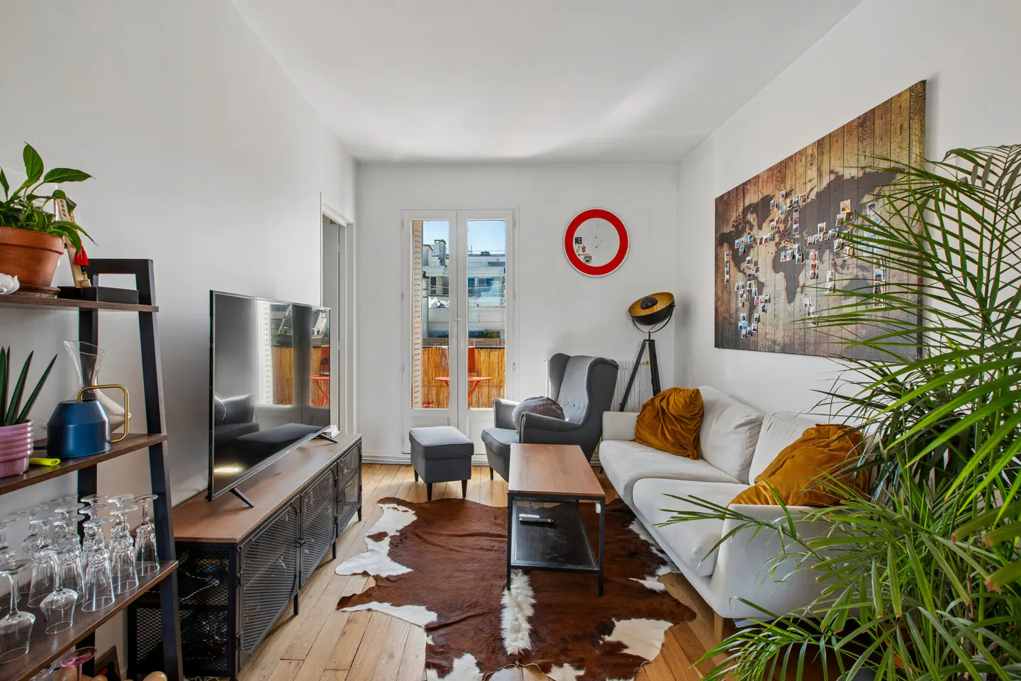 Cozy living room with white walls, wood floors, and a brown and white cowhide rug. A white sofa, gray armchair, and TV stand furnish the space.