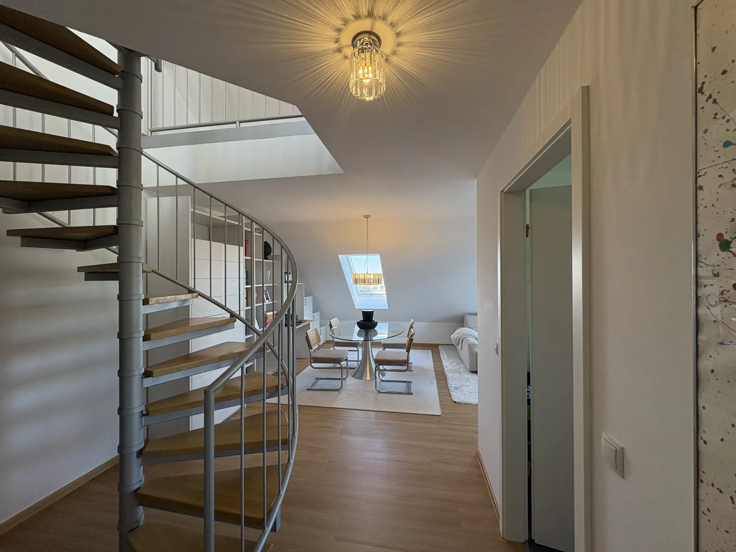 Interior view of a modern apartment with a spiral staircase, dining area with a glass table, and a white sofa.