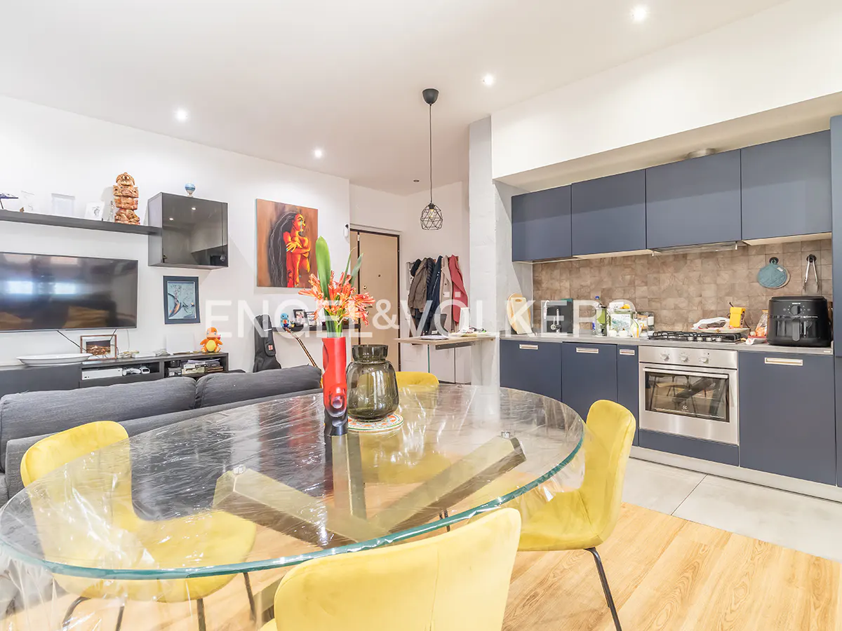 Open-concept living space with a glass table, yellow chairs, gray sofa, and blue kitchen cabinets.
