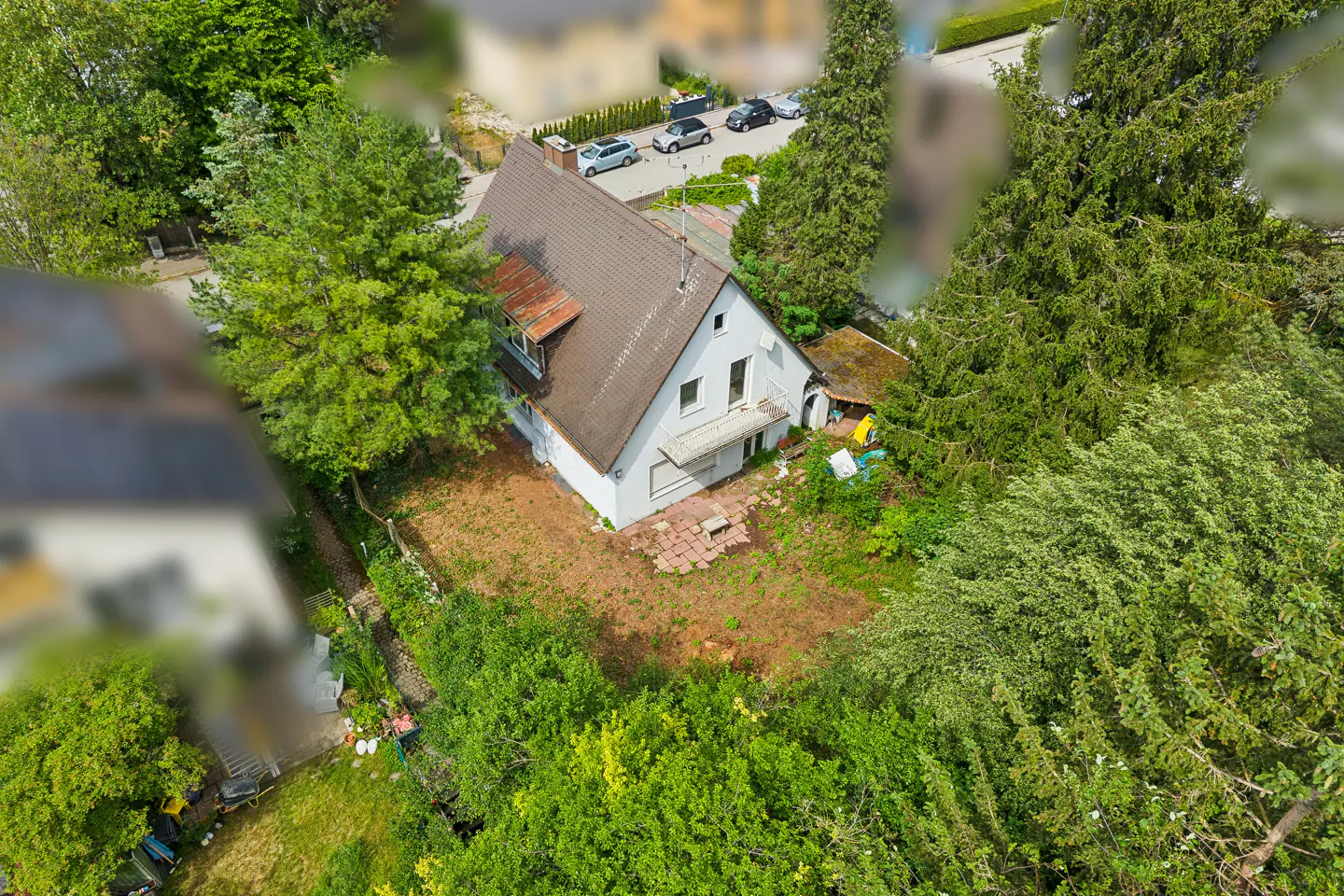 Aerial view of a white house with a brown roof, surrounded by lush green trees and a large, partially cleared yard.