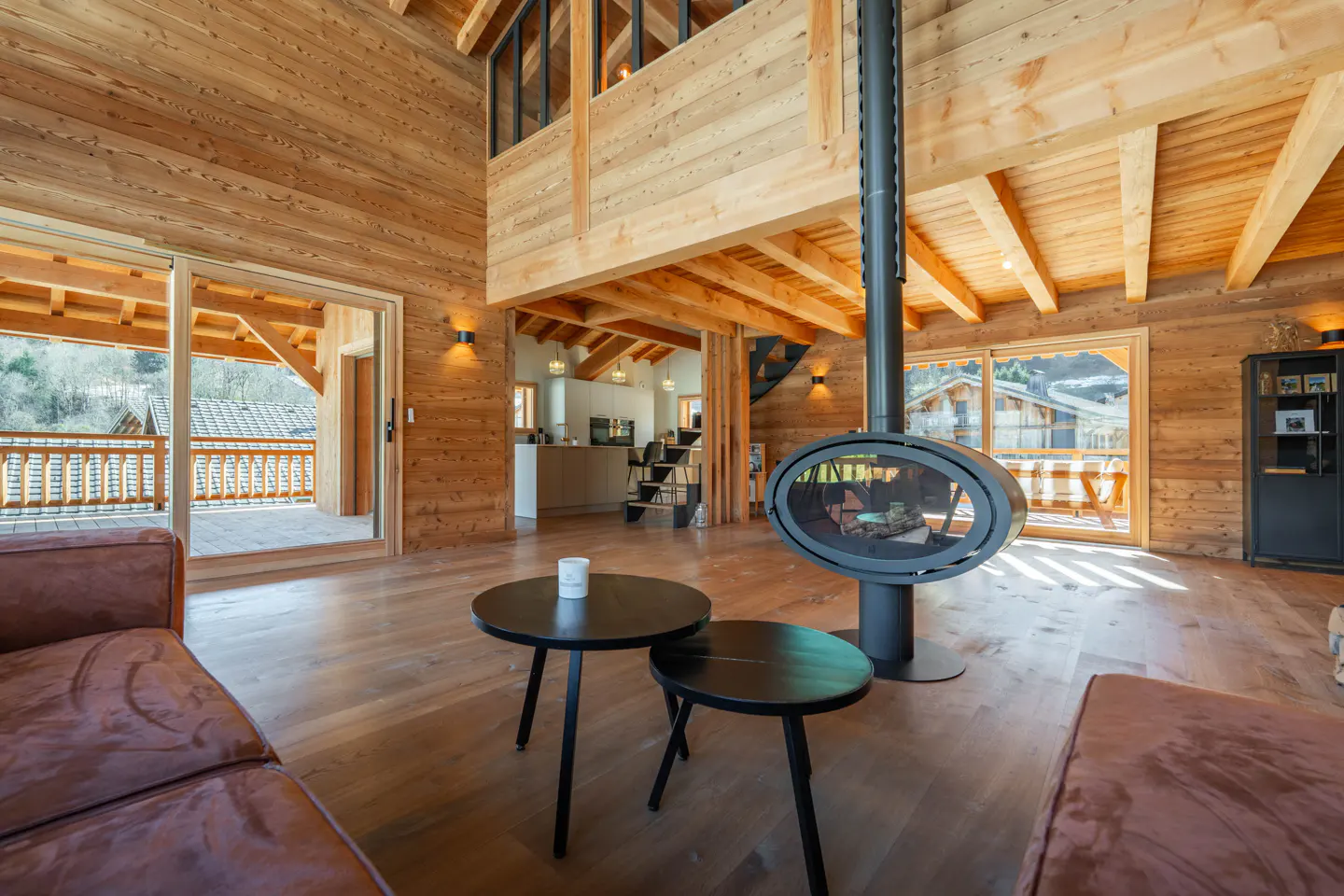 Living room with wood walls, floors, and ceiling. A modern fireplace hangs from the ceiling. Balcony and kitchen visible.